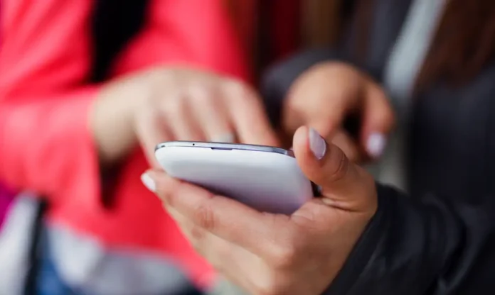 two-beautiful-students-using-mobile-phone-street_0